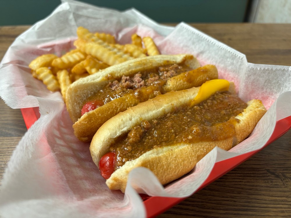 two hot dogs with chili on top, and crinkle fries, in a paper-lined red plastic basket