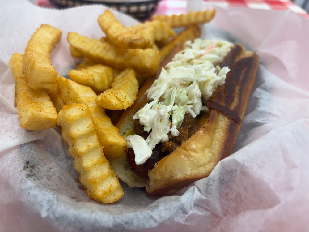 crinkle fries and a chili slaw hot dog in a red plastic basket lined with white paper